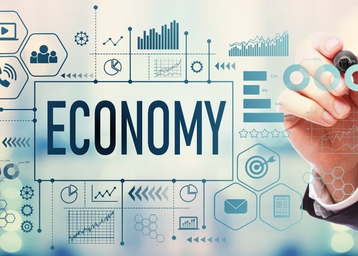The word ECONOMY is prominently displayed amid various financial and data-related icons, charts, and graphs, with a hand holding a marker drawing circular diagrams on the right side.