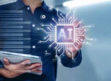 A person in a blue shirt holds a tablet and touches a digital interface displaying a glowing AI chip with circuit lines and technology icons, symbolizing artificial intelligence and innovation.