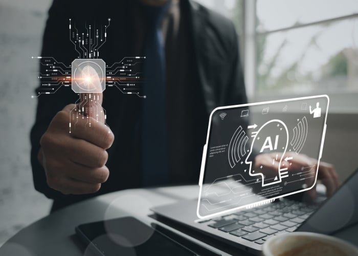 A person in a suit gives a thumbs-up next to a laptop with a digital overlay showing “AI” and circuit graphics, symbolizing artificial intelligence and technology integration.