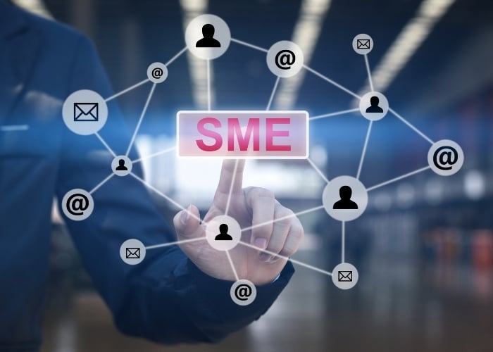 A person presses a virtual button labeled SME, surrounded by icons of people, email, and @ symbols connected by lines, symbolizing small and medium-sized enterprise networking.