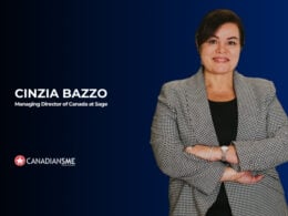 A woman with dark hair in a gray checkered blazer stands smiling with arms crossed on a blue background. Text reads: Cinzia Bazzo, Managing Director of Canada at Sage. CanadianSME.