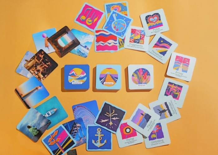 A variety of colorful cards with abstract designs and photos are arranged in an oval shape on an orange surface. Three square cards are placed in the center, surrounded by rectangular cards.