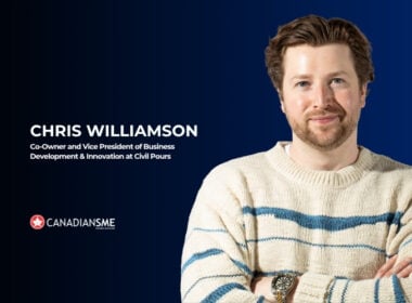 A man with light brown hair and a beard, wearing a cream sweater with blue stripes, stands with arms crossed, smiling. Text reads: Chris Williamson, Co-Owner and Vice President... CanadianSME.