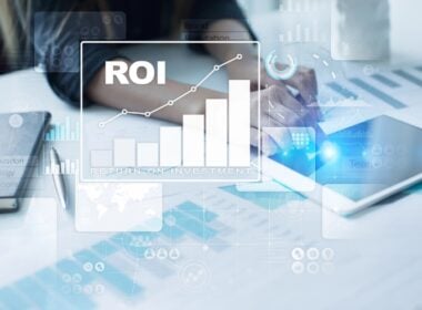 Person working at a desk with a tablet and documents. A digital graphic overlay shows a bar chart labeled ROI (Return on Investment) with an upward trend, representing financial growth or business analysis.