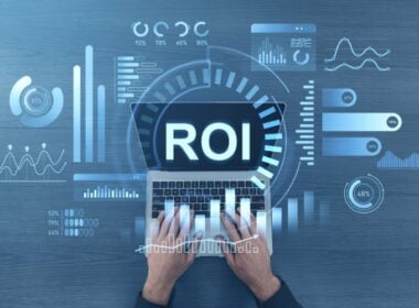 Hands typing on a laptop displaying “ROI” on the screen, with various digital data charts, bar graphs, and analytics icons overlaid, representing financial analysis and return on investment.